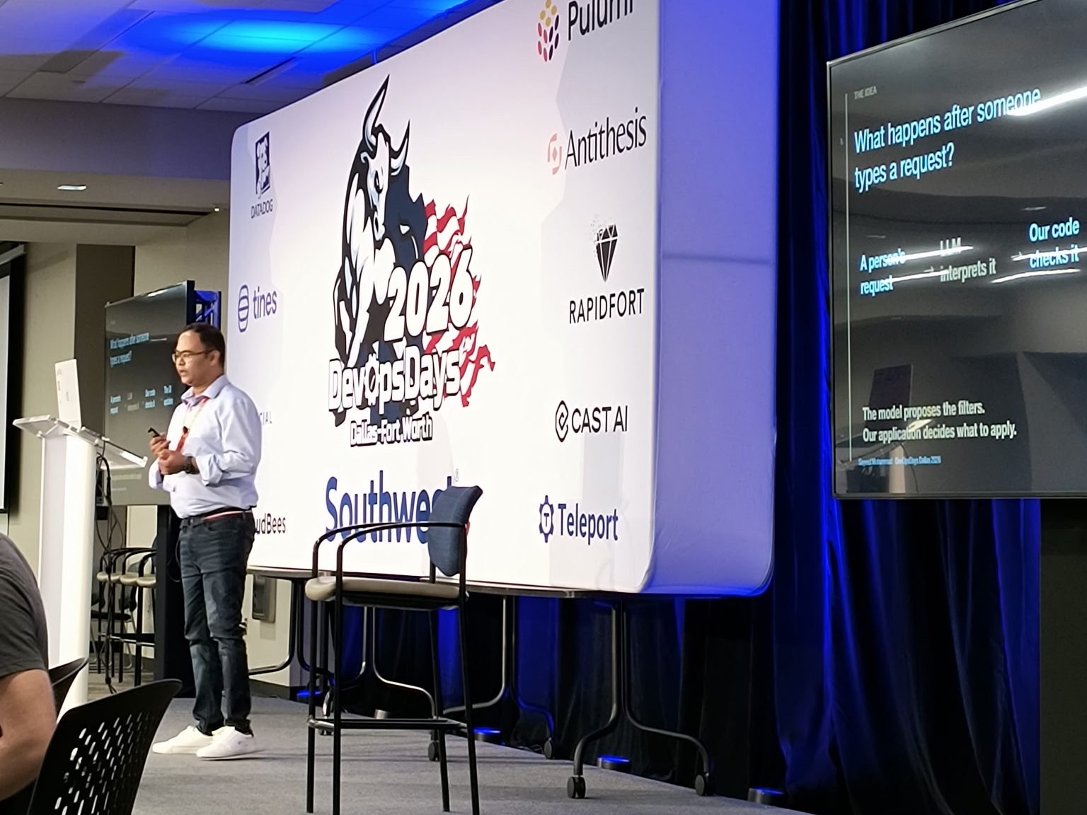 Sayeed Mohammad presenting at DevOpsDays Dallas-Fort Worth 2026, beside a slide reading “The model proposes the filters. Our application decides what to apply.”